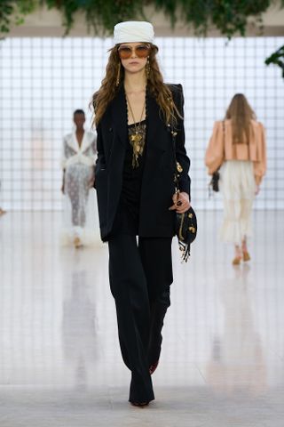 A model wearing a black suit and white pillbox hat at the Chloé S/S 25 runway show.